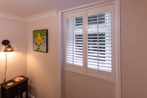 A room with a window with blinds, a wall-mounted lamp, and a framed artwork.