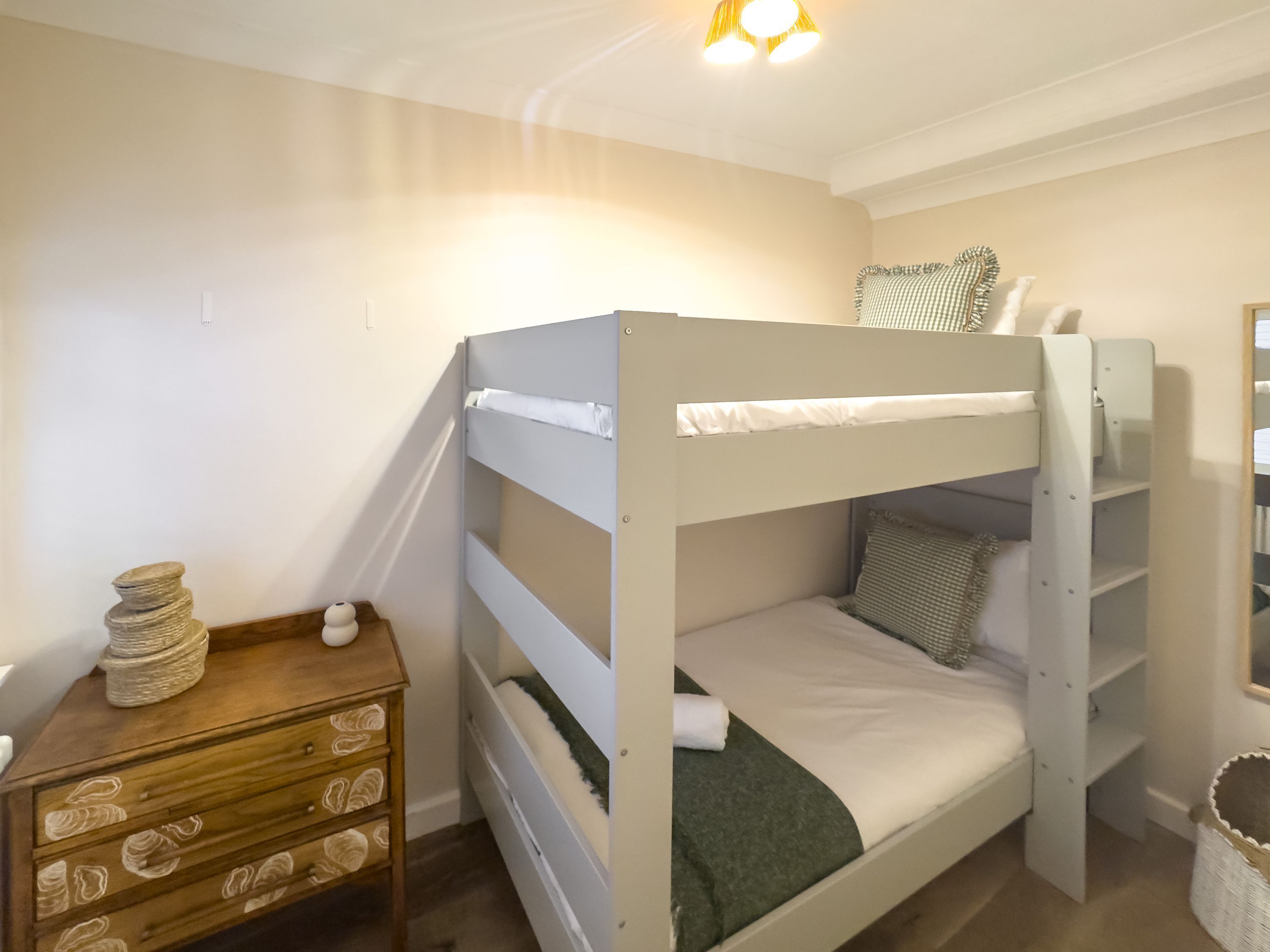 A bunk bed with a wooden dresser and a small table beside it.