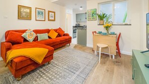 A compact living space with a red sofa, a small dining table, and a kitchen area in the background. - Cosy 2 Bed Viking Bay Cottage (Broadstairs)