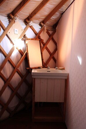 Ein kleines Schlafzimmer im Dachgeschoss mit Holzbalkendecke, einem Fenster und einem schlichten weißen Waschbecken.