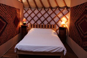 Un lit dans une chambre aux murs décorés de motifs et dotée d’une tête de lit en bois, de deux lampes de chevet et d’une structure de plafond rappelant une tente.