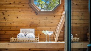 A wooden cabin interior with a skylight, a window, and a shelf with towels and a cocktail glass.