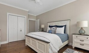 Ein Schlafzimmer mit einem Bett, Nachttischen, einer Lampe, einem Deckenventilator und einer Tür.