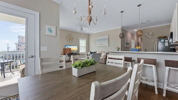 A dining area with a wooden table, white chairs, a chandelier, and a view of the outside. - Residence 201N at The Sandcastle Condominiums (Wildwood Crest)