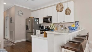 A modern kitchen with white cabinets, a stainless steel refrigerator, a microwave, and a large island with stools. - Residence 201N at The Sandcastle Condominiums (Wildwood Crest)