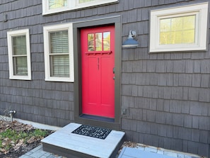 A house with a red door, two windows with shutters, and a small porch with a metal step.