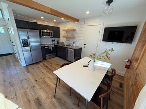 A modern kitchen with stainless steel appliances, a white dining table, and a mounted TV.
