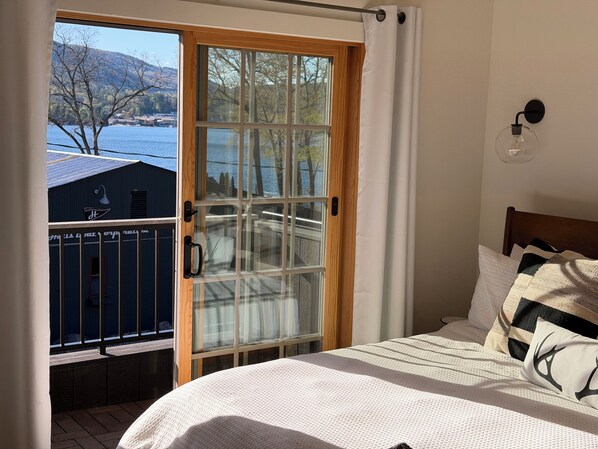 A bedroom with a bed, a window with a view of a lake and buildings, and a curtain.