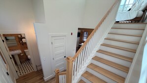 A staircase with wooden steps and white railings, leading to a bedroom with a bed and a window. - Deluxe Lodge Lakefront On Lake George #11 (Lake George)