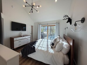 Un dormitorio con cama, televisión, cómoda, candelabro y ventana con vistas.