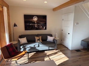 A modern living room with a grey sofa, a red and black chair, a floor lamp, and a painting of fireworks.