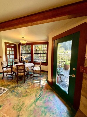 Uma área de refeições com mesa, cadeiras, janelas amplas e uma porta verde.