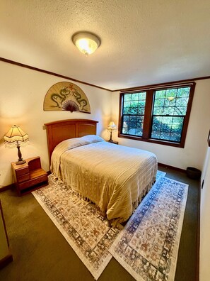 Um quarto com uma cama, mesa de cabeceira, abajur, janela e um leque decorativo.