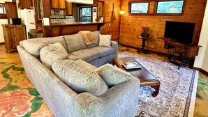 Un salon chaleureux avec un canapé, une table basse, un tapis, des murs en bois et un téléviseur.