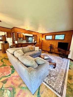 Ein gemütliches Wohnzimmer mit einer Couch, einem Couchtisch, einem Teppich, Holzwänden und einem Fernseher.