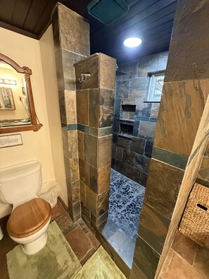 Een badkamer met een douchecabine van steen, een houten toilet en een spiegel.