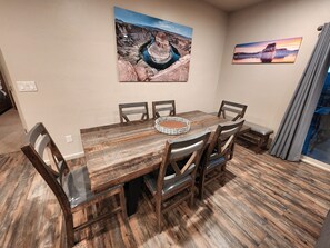 A dining area with a wooden table, six chairs, and two wall-mounted paintings. - The Desert Dip Oasis at Lake Powell with swim spa!
 (Page)