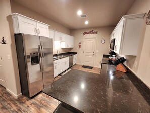 A modern kitchen with white cabinets, a stainless steel refrigerator, a black countertop, and a 'gather' sign on the wall. - The Desert Dip Oasis at Lake Powell with swim spa!
 (Page)