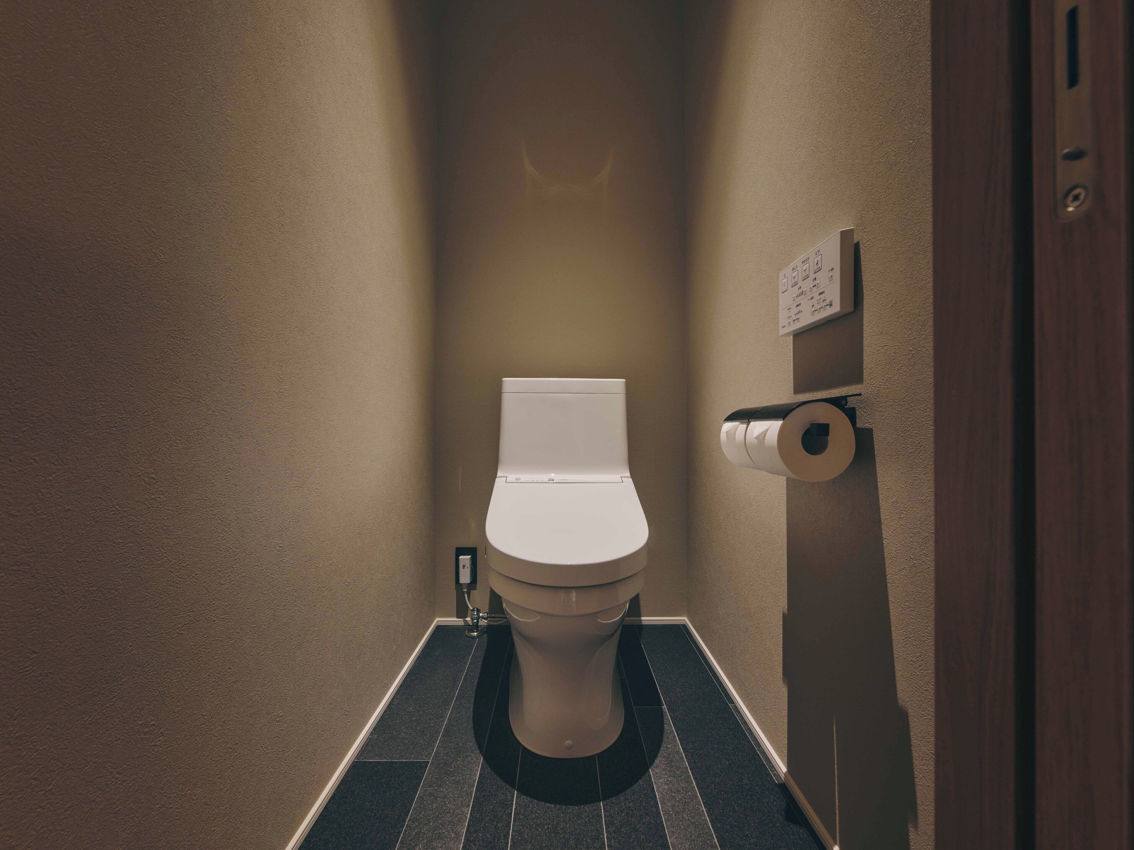 A toilet with a roll of toilet paper on the wall, a wall-mounted sign, and a tiled floor.