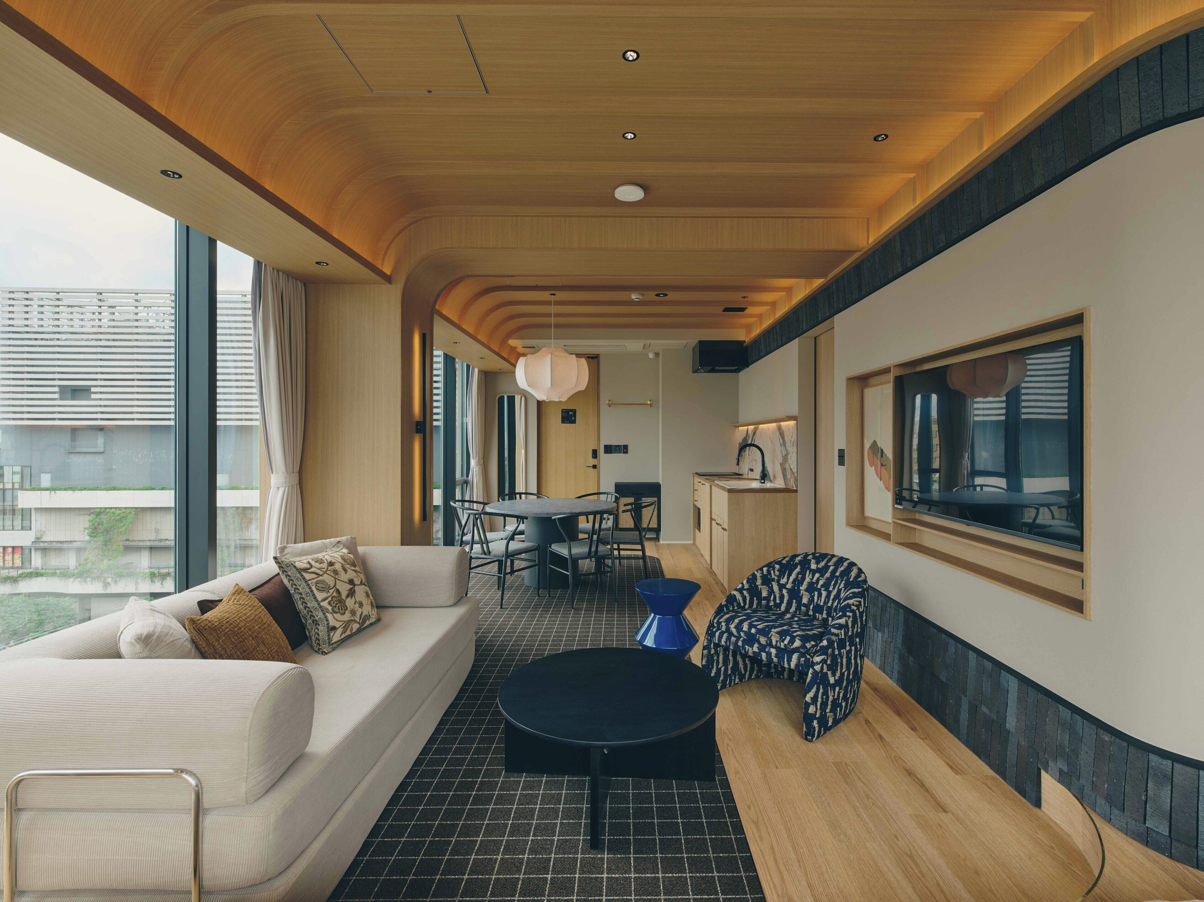 Un interior moderno con un sofá, una mesa de comedor y sillas, una zona de cocina y ventanas amplias con vistas.