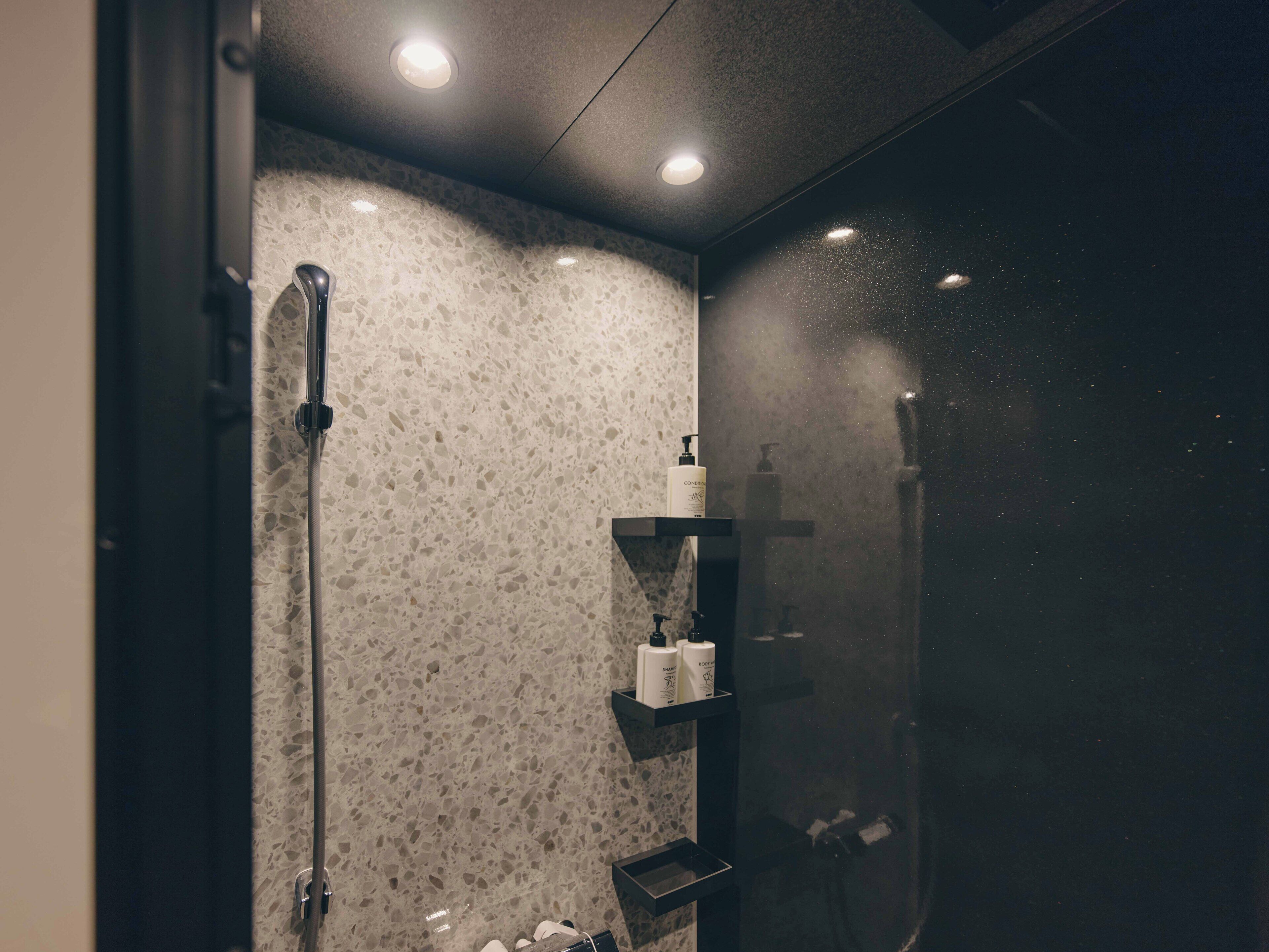 Uma casa de banho moderna com chuveiro, espelho e prateleira com produtos de higiene pessoal.