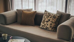 Un sofá con cojines estampados, una mesita con una taza y un libro, y una ventana con cortinas al fondo.