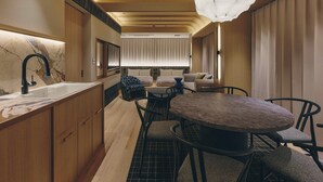 Una habitación de hotel moderna con una zona de cocina, una mesa de comedor con sillas y un amplio ventanal con cortinas.