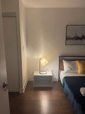 Ein Schlafzimmer mit einem Bett, einem Nachttisch mit Lampe, einer Tür und einem Wandbild.