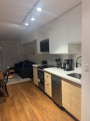 Eine kleine Küche mit weißen Schränken, Backofen, Geschirrspüler und Kaffeemaschine.