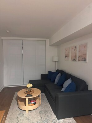 Ein modernes Wohnzimmer mit einem dunkelgrauen Sofa, einem runden Couchtisch mit Büchern, einer Vase mit Blumen und einem Schiebetürenschrank.