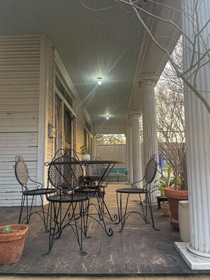 A covered porch with a table and chairs, potted plants, and a view of the street. - Room with Private Entrance in Antique Victorian Artist House (Dallas)