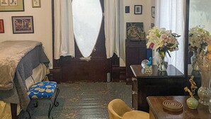 Een kamer met een bed, een klein tafeltje met een bloemetjesvaas, een stoel, een houten kast en een spiegel.