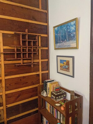 A wooden bookshelf with books and a small figurine, a ladder against a wooden wall, and two framed pictures on the wall. - Room with Private Entrance in Antique Victorian Artist House (Dallas)