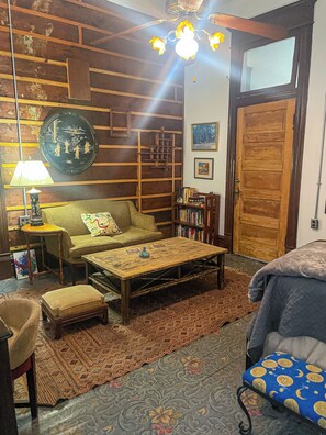 A cozy living room with a sofa, a coffee table, a bookshelf, and a wooden ceiling. - Room with Private Entrance in Antique Victorian Artist House (Dallas)