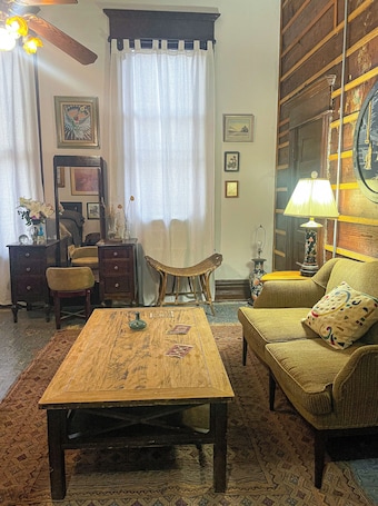 A living room with a wooden coffee table, a sofa, a chair, a lamp, and a large mirror.. Room with Private Entrance in Antique Victorian Artist House