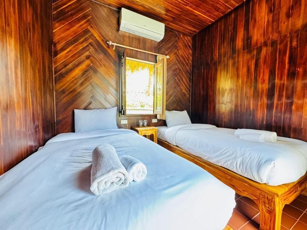 A room with two beds, wooden walls, a window, and an air conditioning unit.