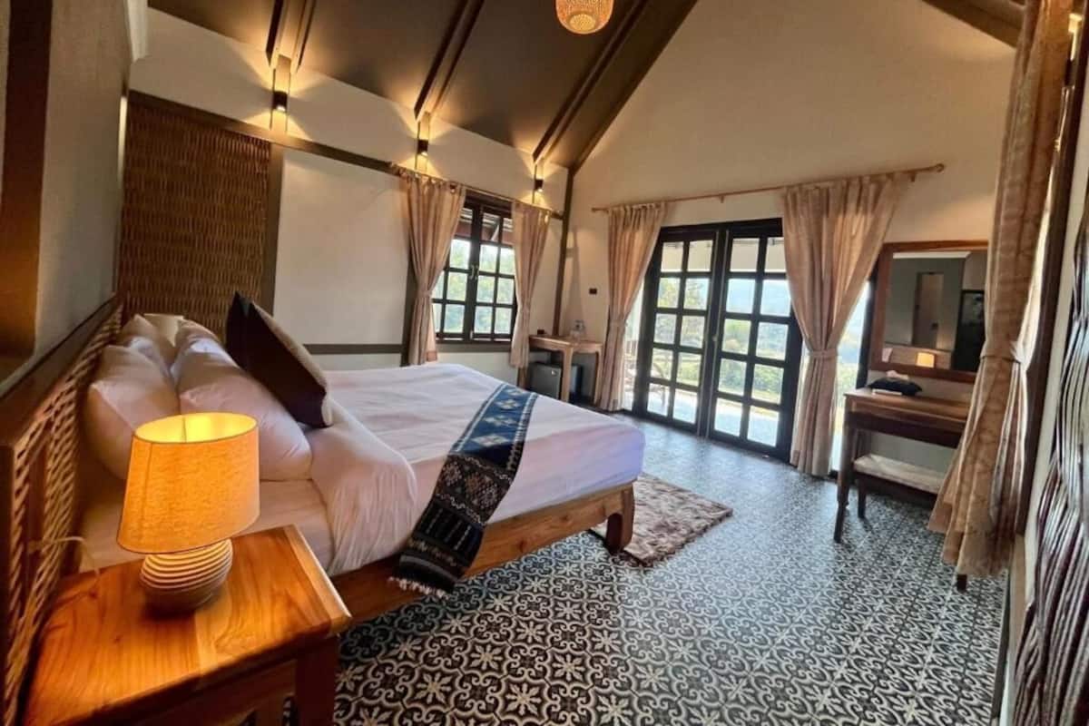 A bedroom with a bed, bedside lamp, curtains, and a view of the outdoors.