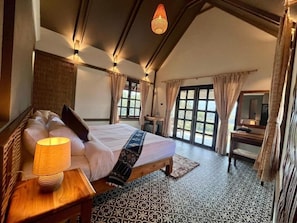 A bedroom with a bed, bedside lamp, curtains, and a view of the outdoors.