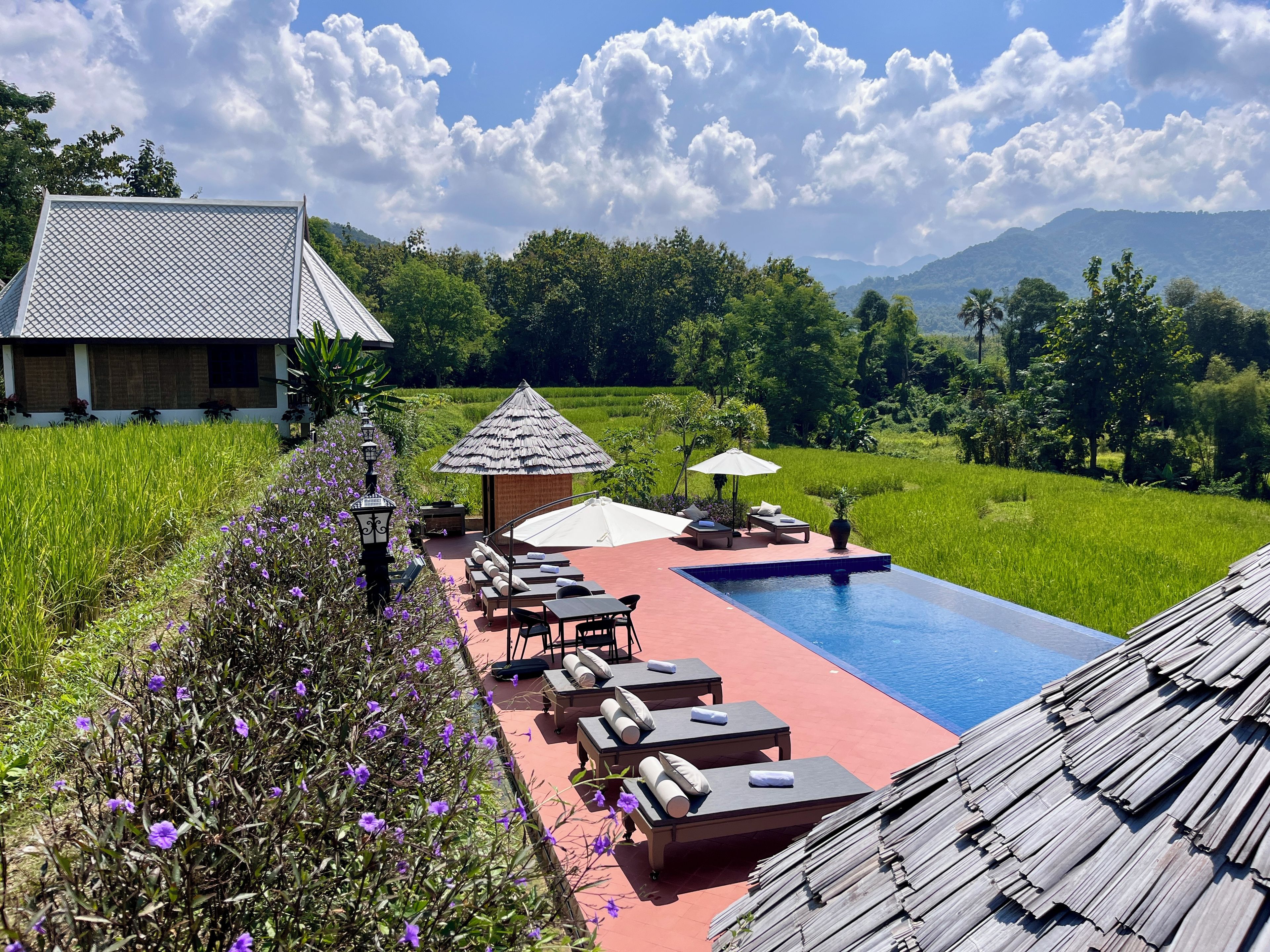 Ein Poolbereich mit Liegestühlen und einer kleinen Laube, umgeben von üppiger Vegetation und Blick auf ferne Berge.
