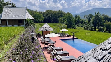 Ein Poolbereich mit Liegestühlen und einer kleinen Laube, umgeben von üppiger Vegetation und Blick auf ferne Berge.