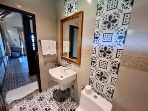 A bathroom with a sink, mirror, toilet, patterned tiles, and a doorway leading to a hallway. - Kuangsi Resort (Luang Prabang)