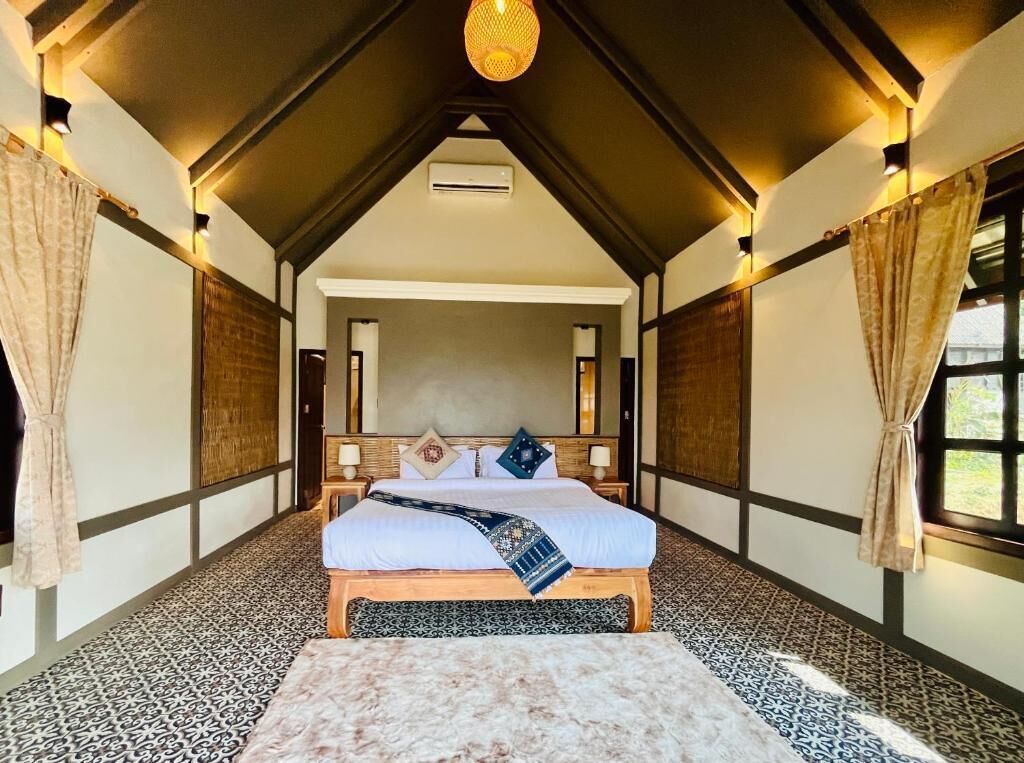 A bedroom with a bed, a wooden headboard, a hanging light fixture, and a window with curtains.