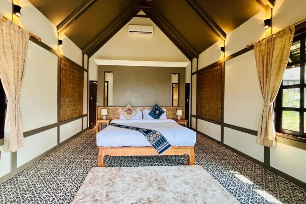 A bedroom with a bed, a wooden headboard, a hanging light fixture, and a window with curtains.