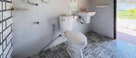 Un baño con inodoro, bidé y lavamanos, suelo de baldosas y vistas al exterior.