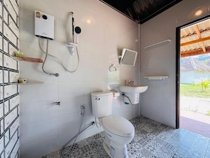 Een badkamer met toilet, bidet en wastafel, betegelde vloer en uitzicht op het groen.