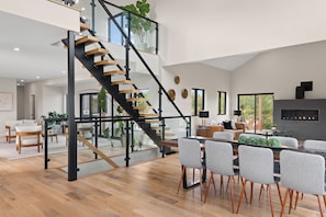A spacious living area with a modern staircase, a dining table with chairs, and a fireplace.