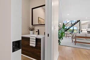 A modern bathroom with a wooden vanity, a mirror, and a potted plant.