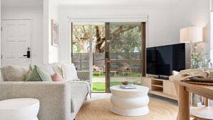 A modern living room with a grey sofa, a round coffee table, a TV, and a sliding glass door leading to a backyard.
