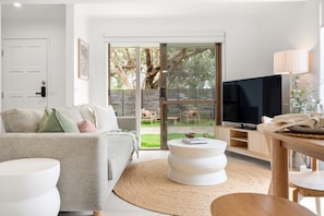 Ein modernes Wohnzimmer mit einem grauen Sofa, einem runden Couchtisch, einem Fernseher und einer Schiebetür zum Garten.