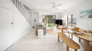 A modern interior with a staircase, a dining area with a table and bench, a sofa, and a TV.